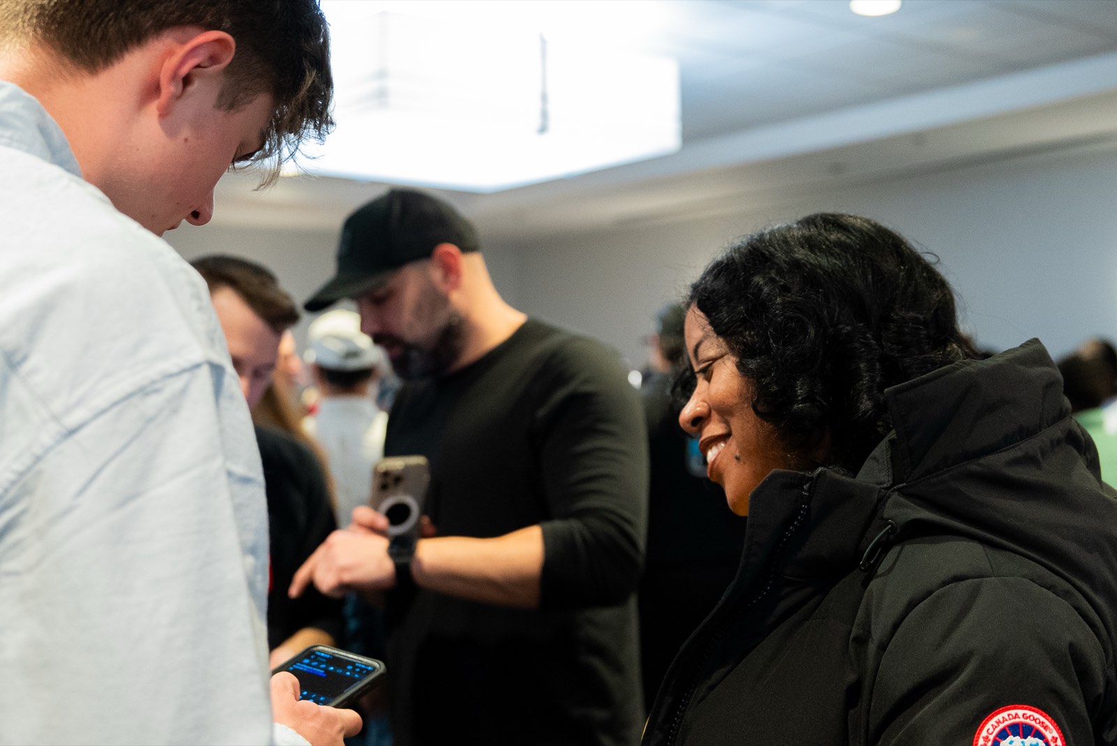 Three attendees compare figures on their phones during a break at a SubTo member meetup; one holds a phone displaying a spreadsheet.