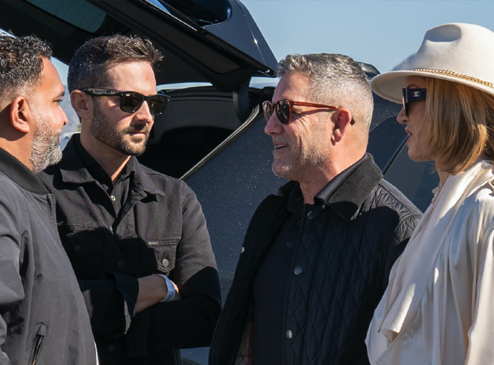 Four members stand talking in bright sun beside an open vehicle at a SubTo gathering.